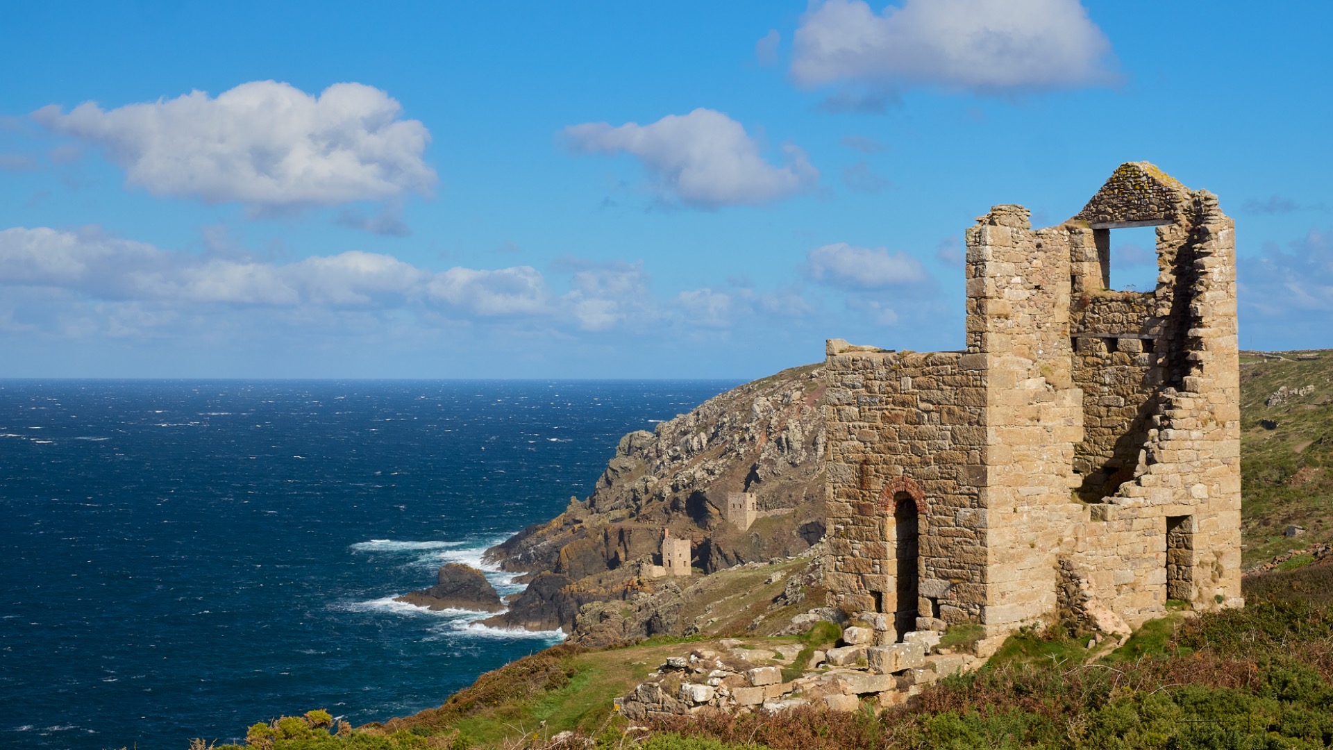 Ruines d'une mine en pierre anciennes sur une falaise, vue sur l’océan Atlantique et un ciel bleu nuageux.