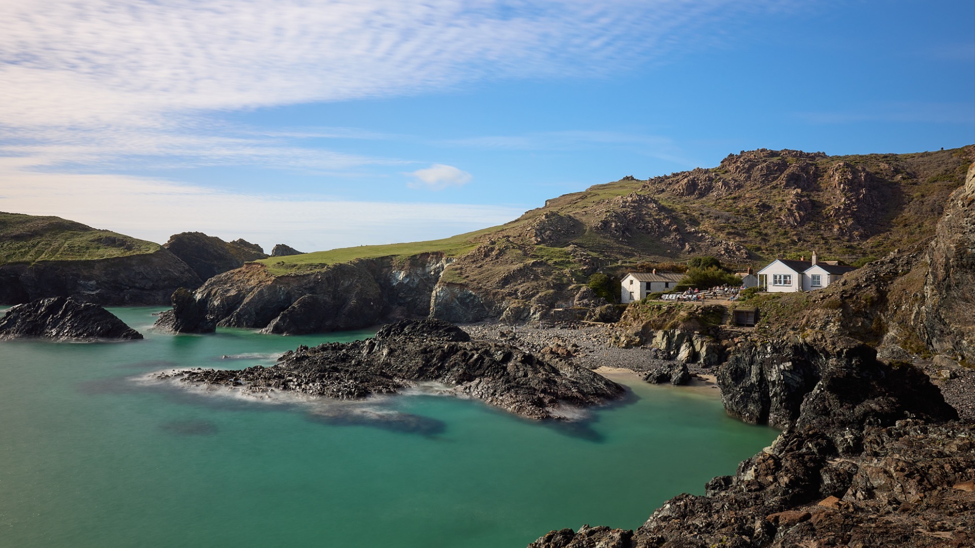 Baie turquoise, falaises rocheuses et maisons blanches au bord d’une plage, sous un ciel bleu.