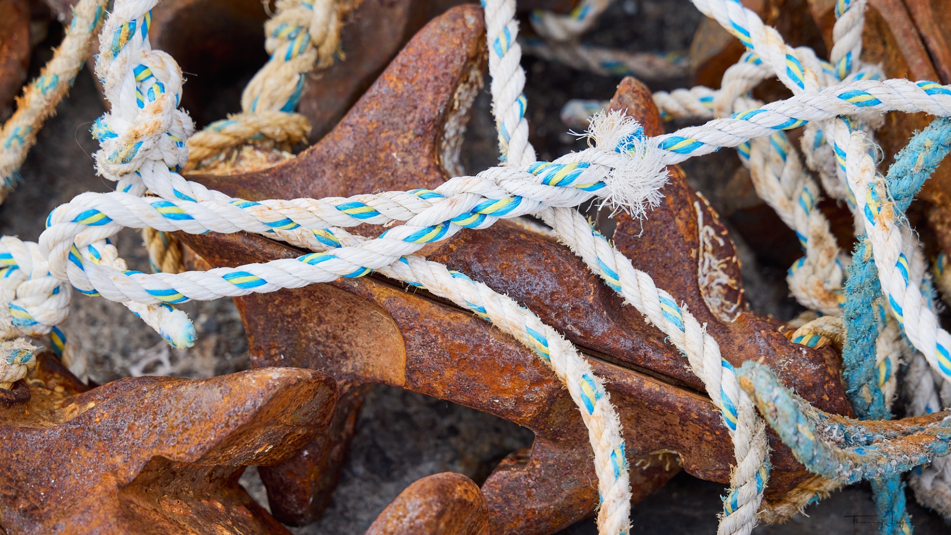 Cordage blanc et bleu noué, gros plan sur butées de cale en métal oxydé et fibres effilochées.