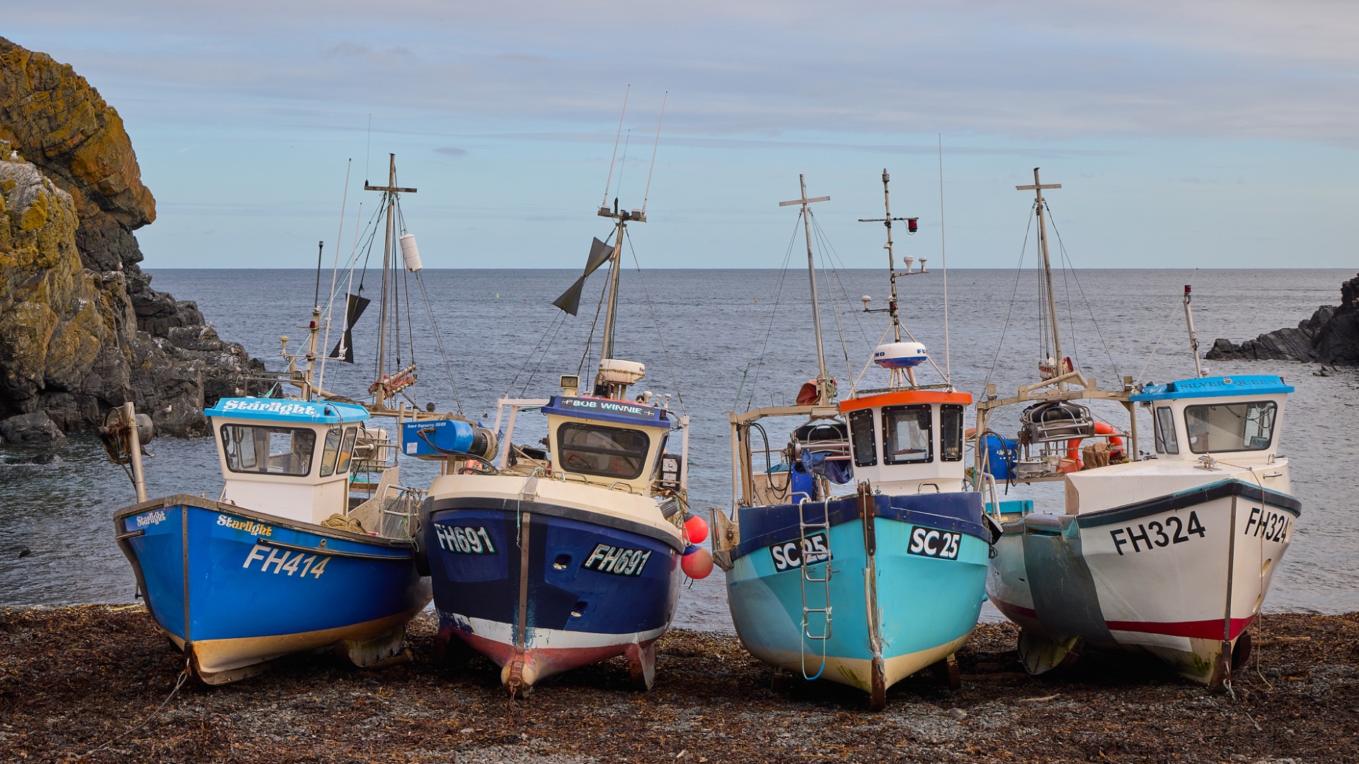 Quatre petits bateaux de pêche colorés amarrés sur une cale rocheuse.